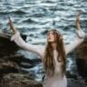 A woman with her hands up in the air by a body of water